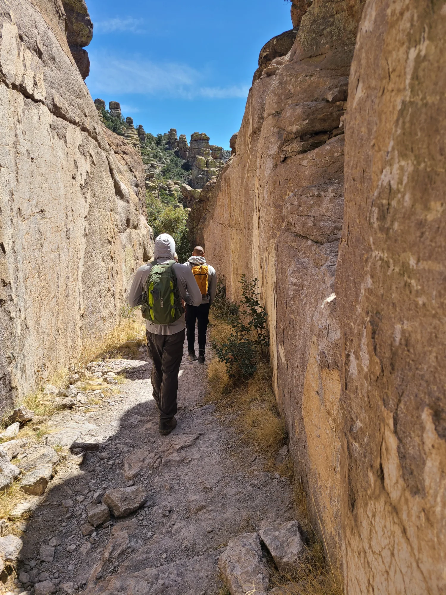 Two hikers walking through a narrow rhyolite passage between tall rock walls on the Echo Canyon Trail